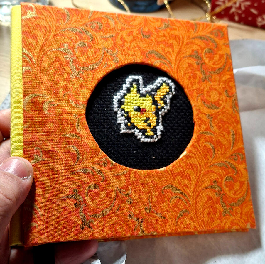 "Pikachu Sketchbook" - 5"x5" sketchbook with cross-stich cover insert. Handbound using three-piece bradel binding